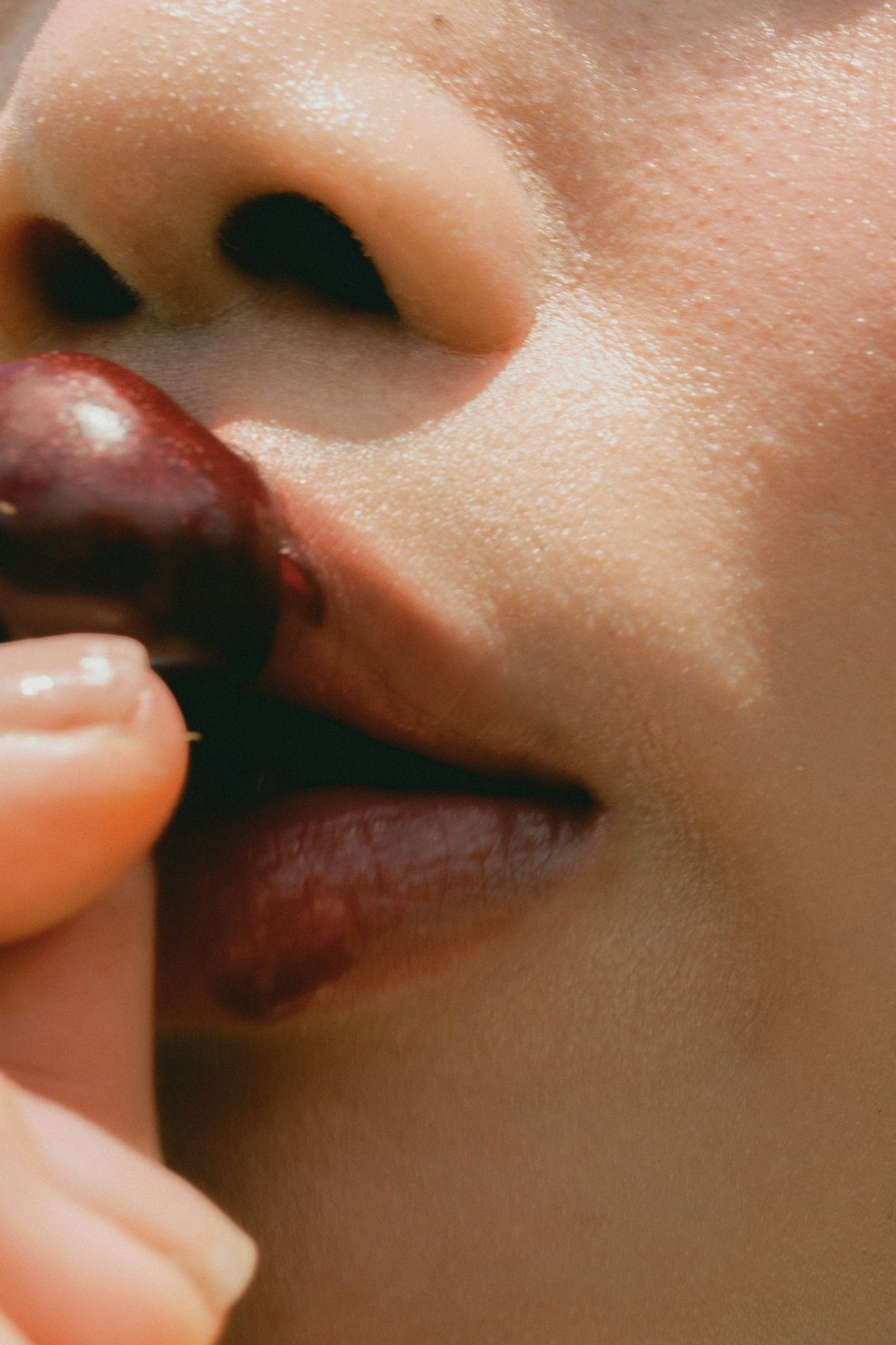 A cherry held to the lips in warm light